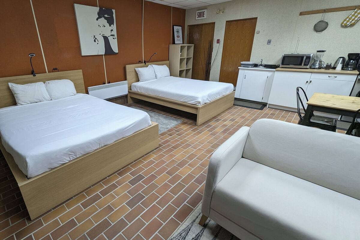 Ein Hotelzimmer mit zwei Einzelbetten, einer Schlafcouch, einer Küchenzeile und einem Badezimmer.