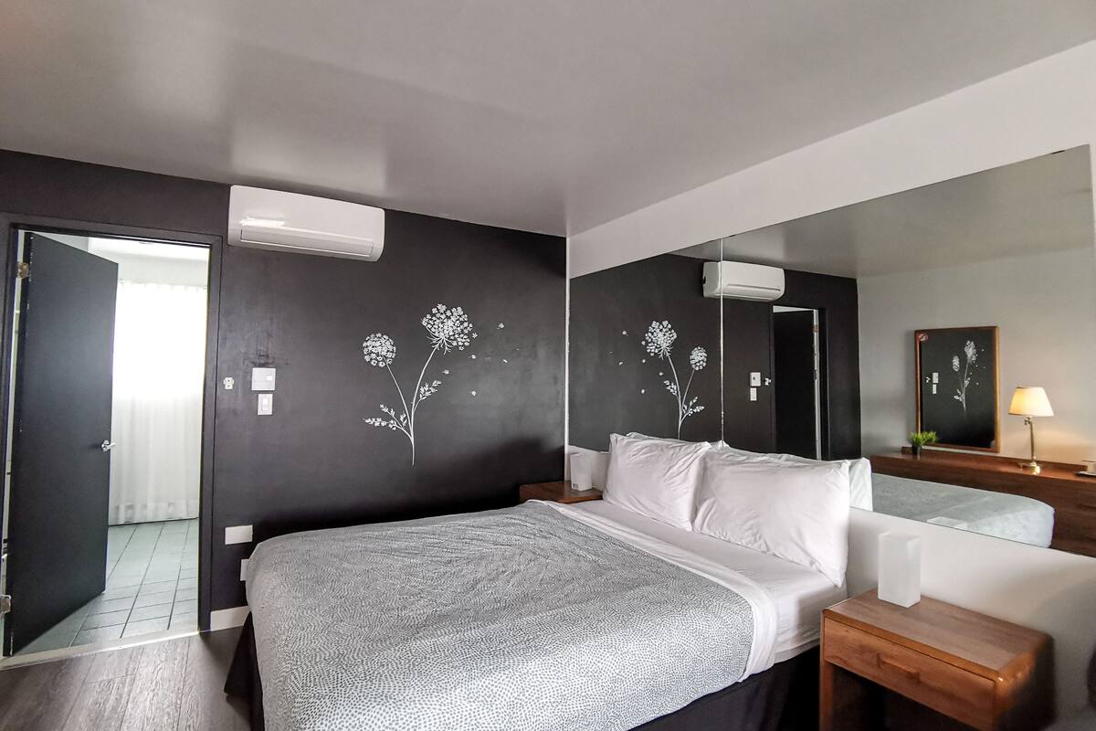 Ein modernes Schlafzimmer mit einem großen Bett, einem Nachttisch, einem Spiegel und einer Wand mit floraler Wandkunst.