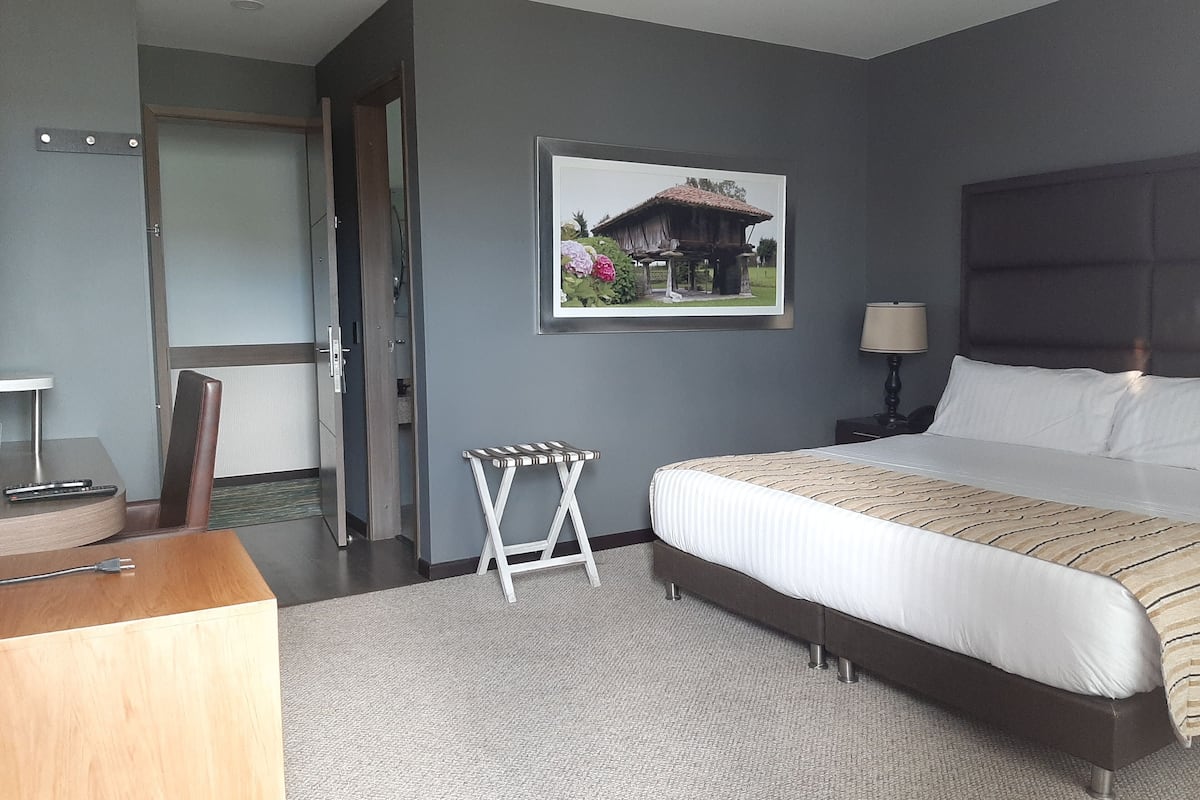Un dormitorio con cama, mesita de noche, lámpara y un cuadro en la pared.