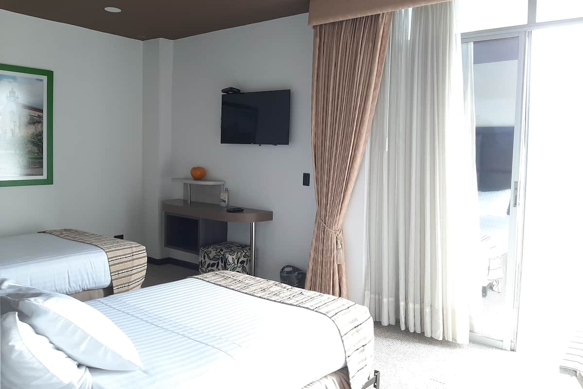 Habitación de hotel con dos camas, un televisor de pantalla plana, una mesita con fruta y un ventanal con cortinas.