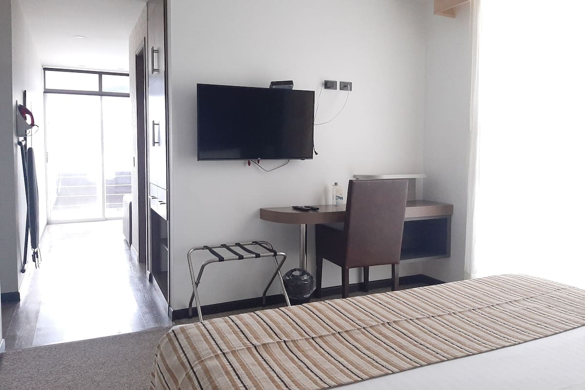 Una habitación de hotel con cama, escritorio, silla, televisor y ventana.