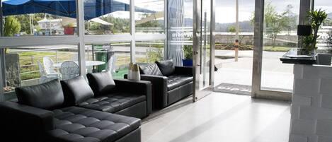 A modern living area with a black sectional sofa, a glass door leading outside, and a view of a green landscape.