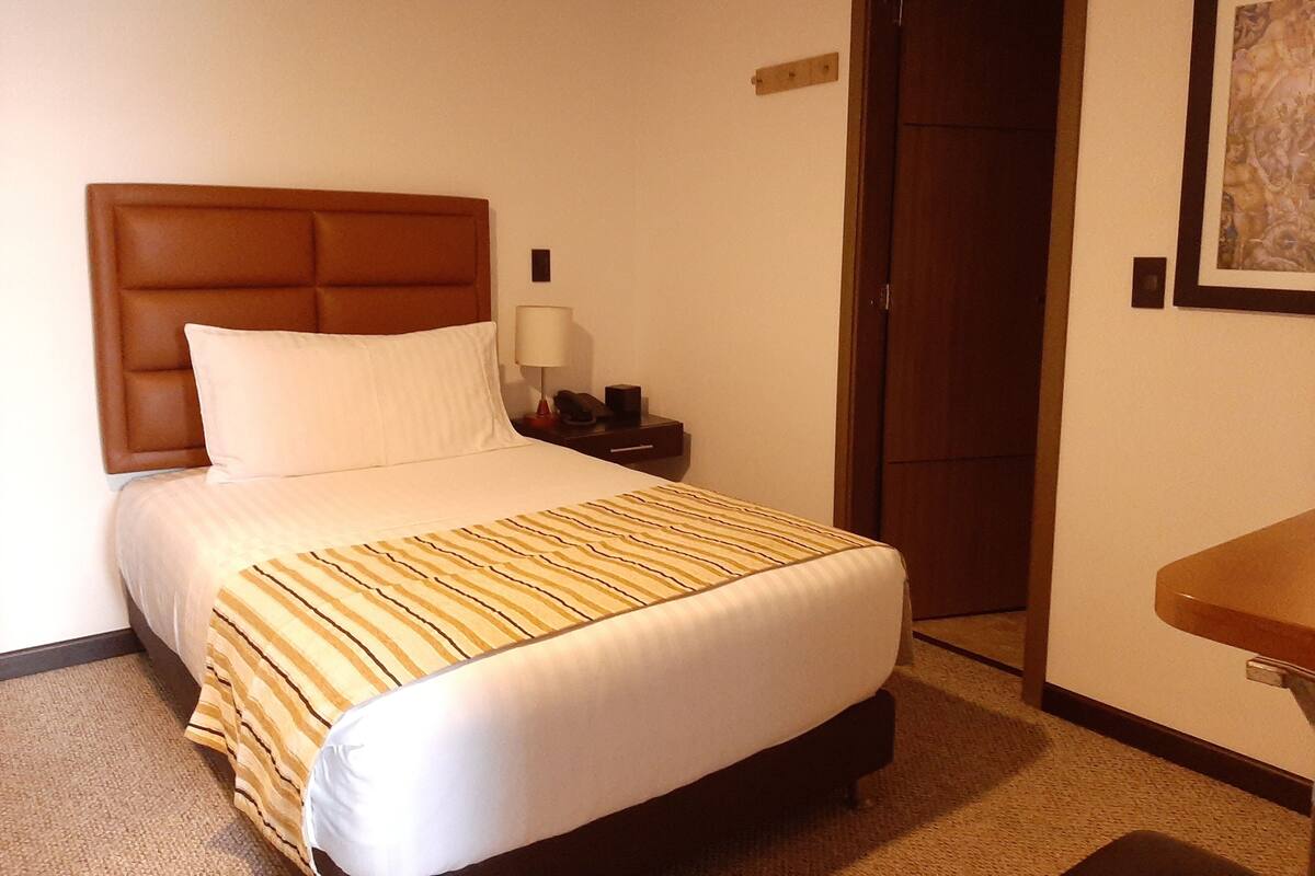 Una habitación de hotel con una cama, una mesita de noche, una lámpara y una puerta.