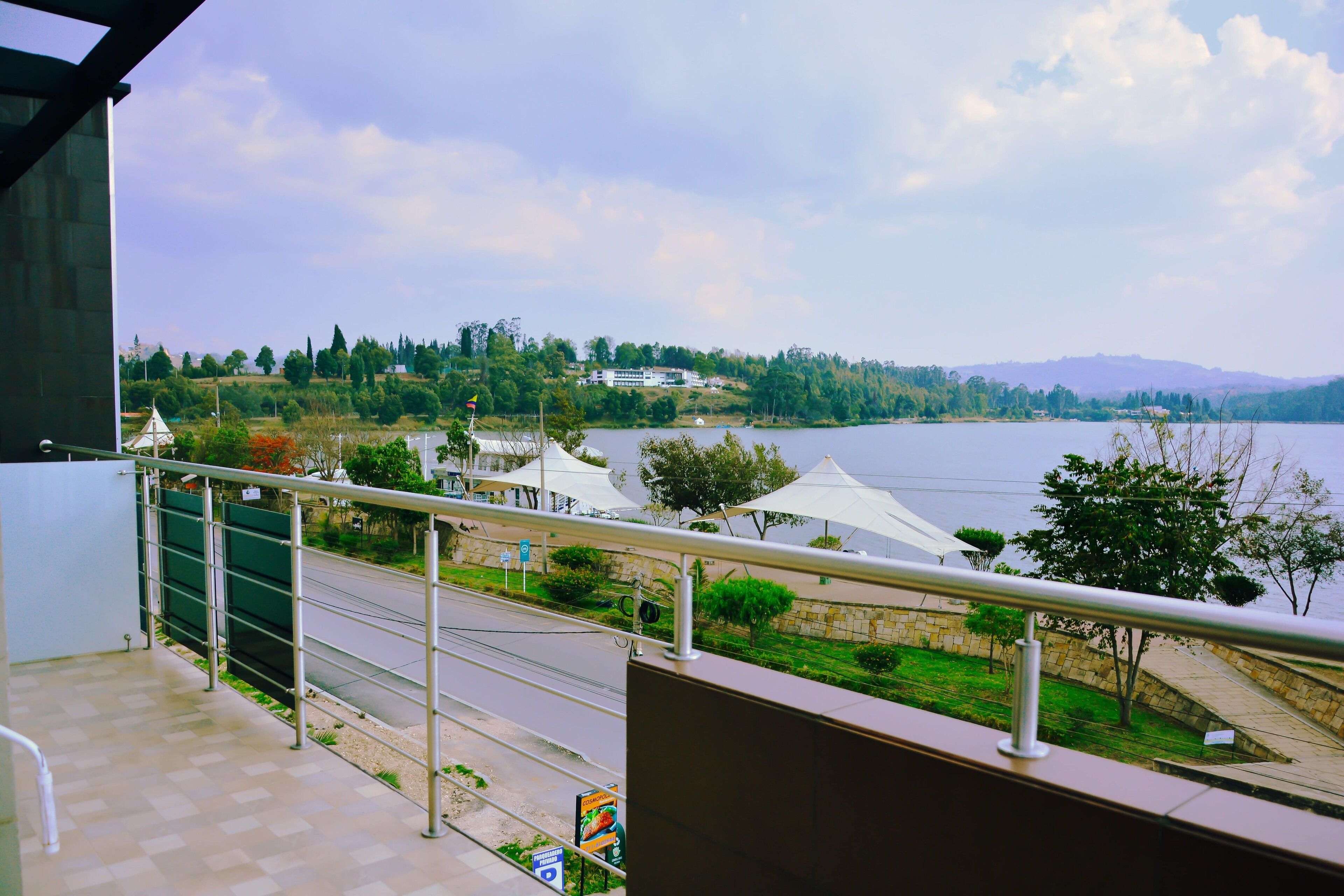 Un balcón con vista a un lago, una carretera y edificios a lo lejos.
