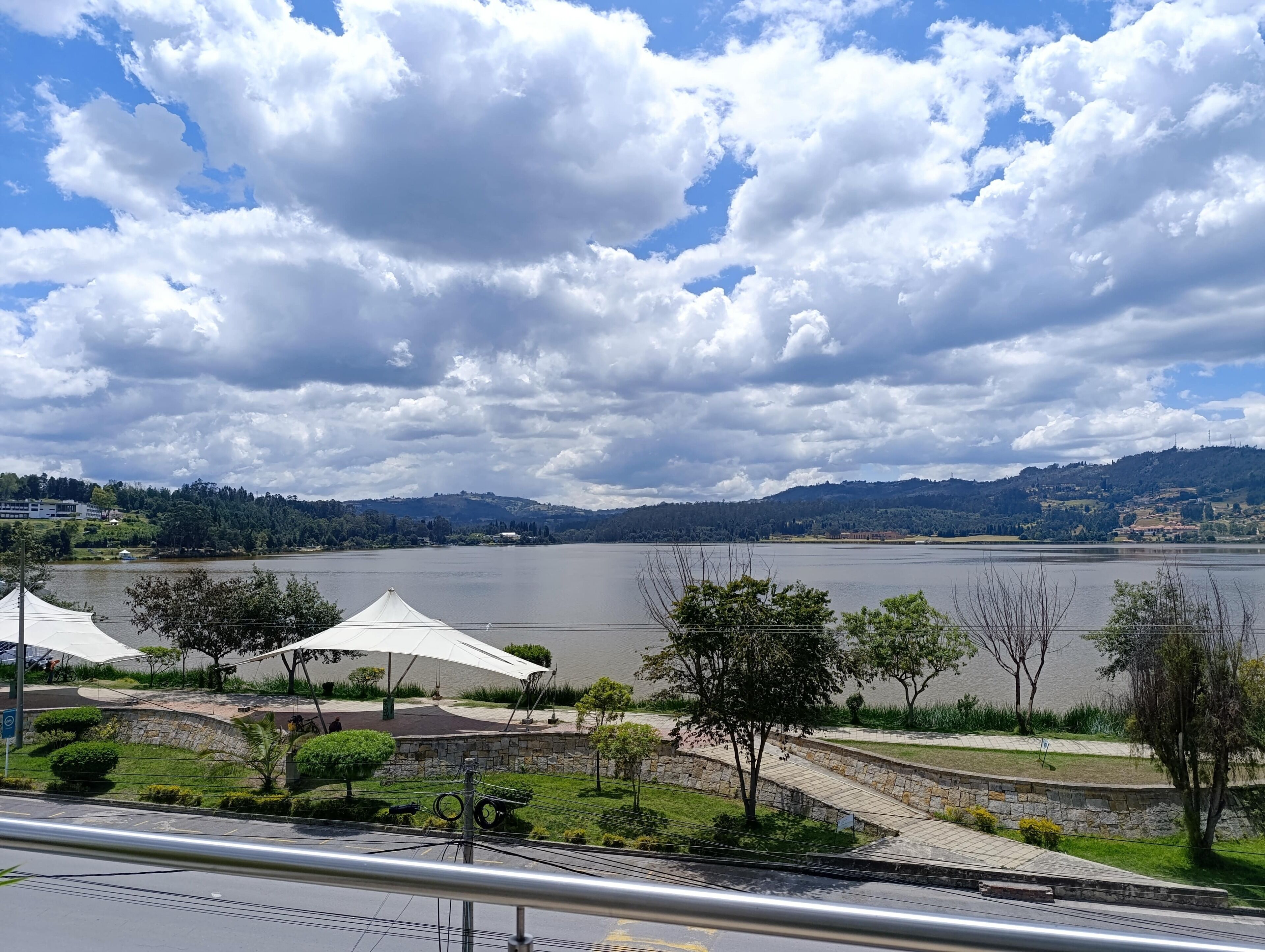 A lakeside view with a stone pathway, trees, and a white tented area.