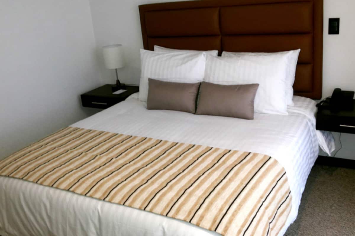 Una cama bien hecha con colcha a rayas, un cabecero de madera y una mesita de noche con lámpara.