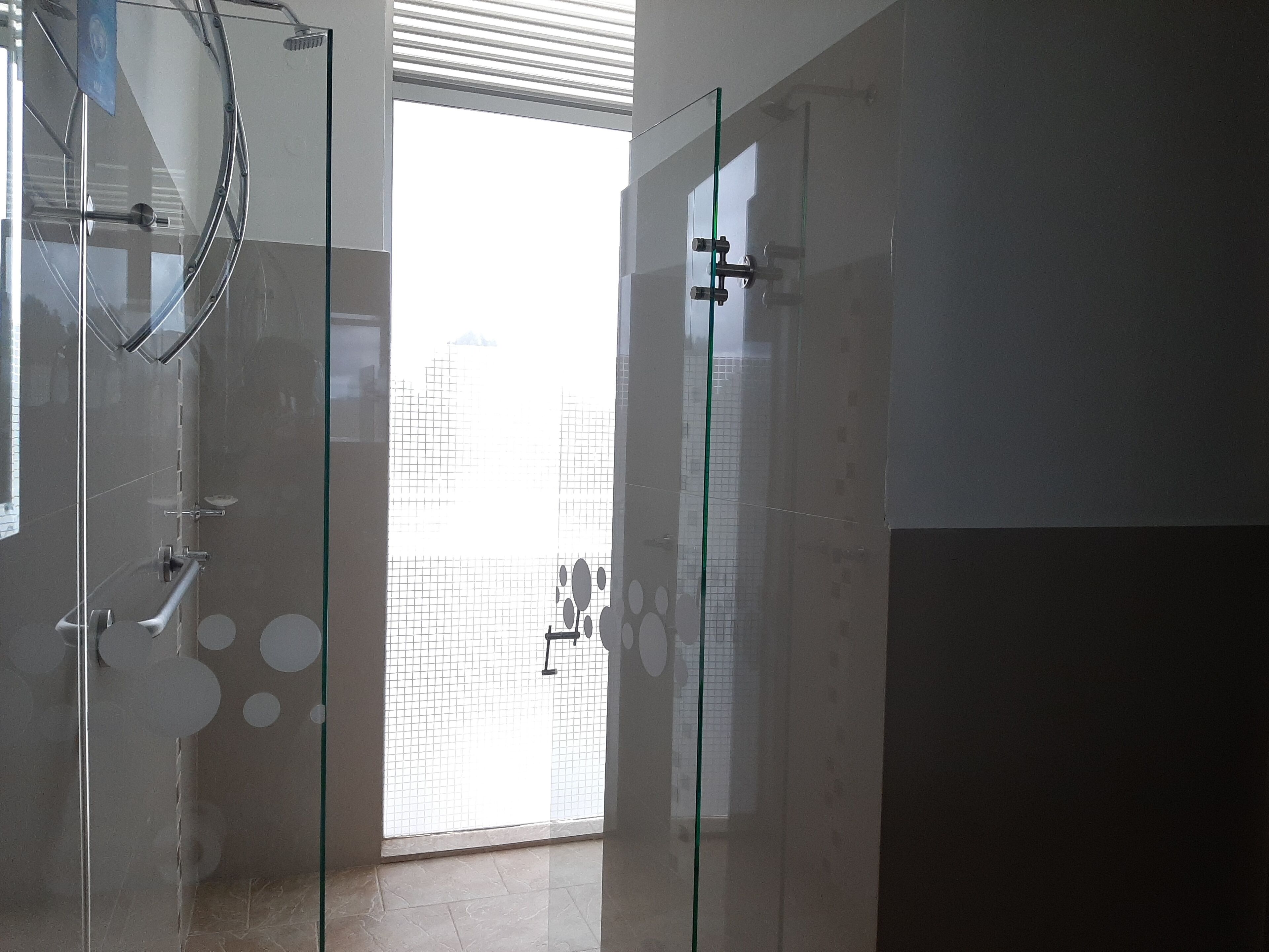 Un baño moderno con cabina de ducha de vidrio, ventana visible y suelo de baldosas.