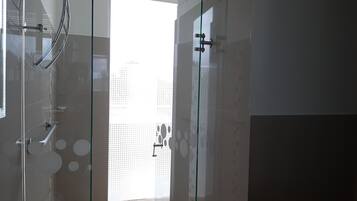 Un baño moderno con cabina de ducha de vidrio, ventana visible y suelo de baldosas.
