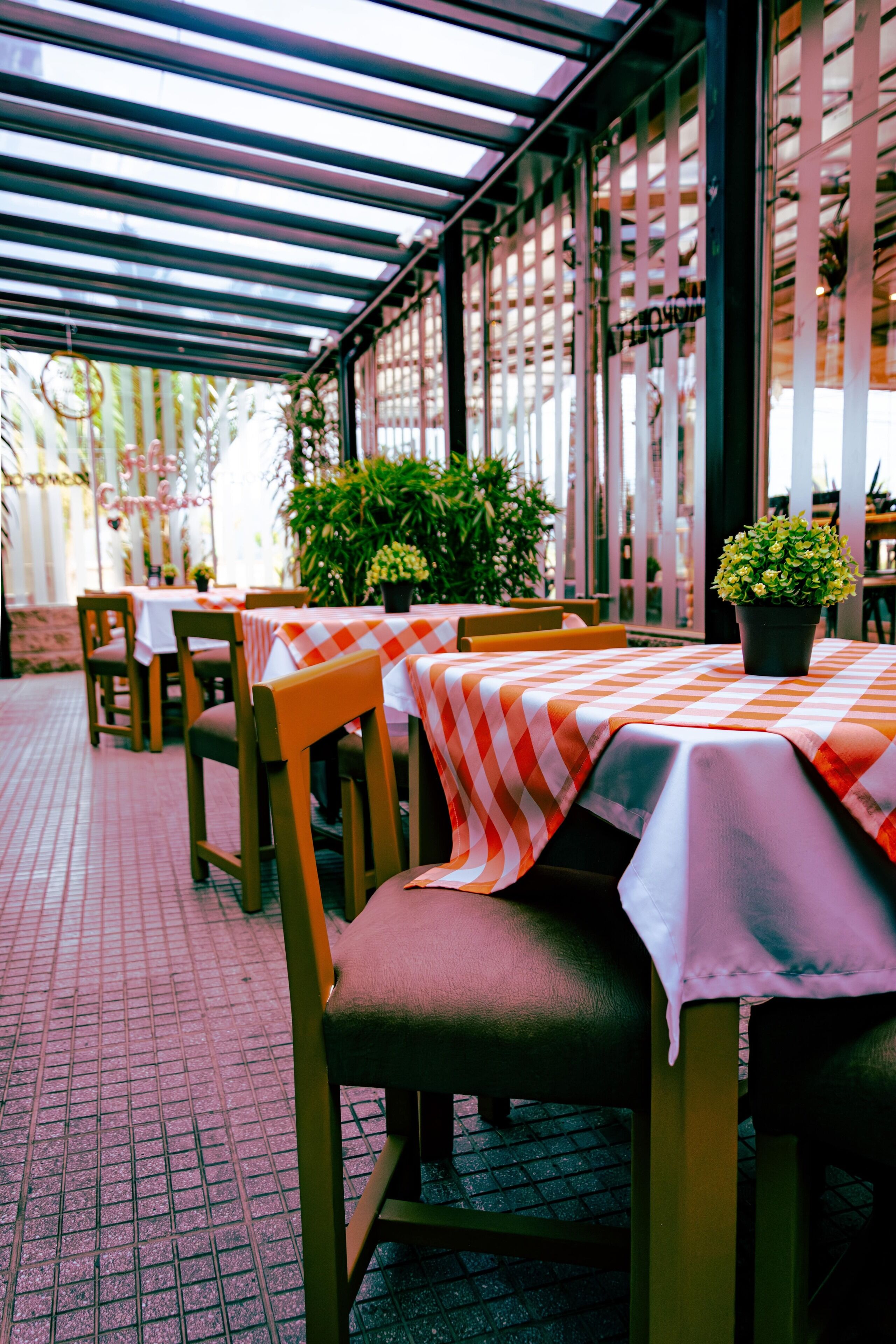Un espace extérieur aménagé pour les repas, avec des tables recouvertes de nappes à carreaux, des chaises en bois et des plantes en pot.