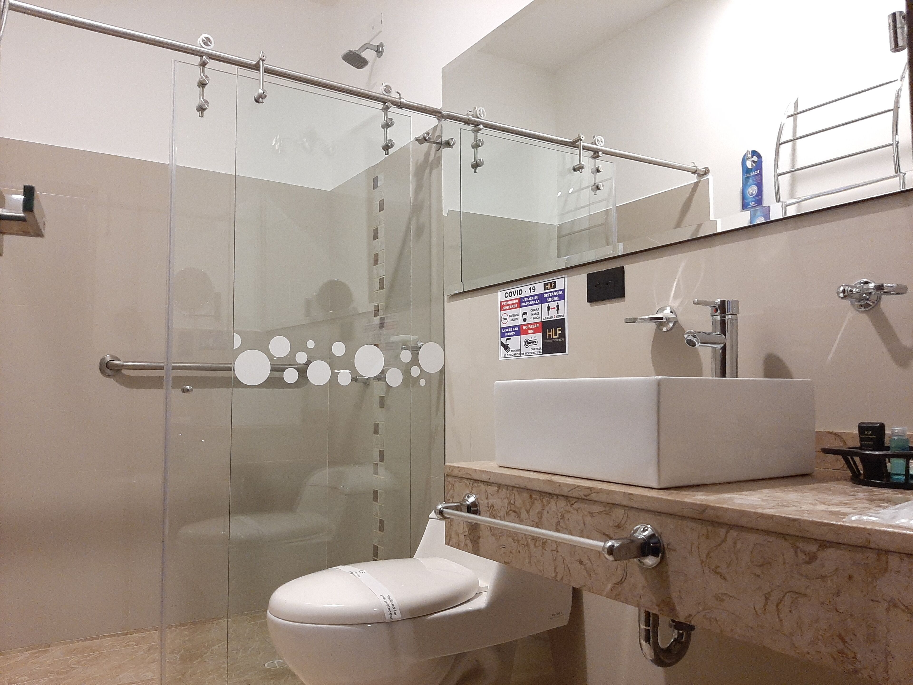 Un baño moderno con cabina de ducha de vidrio, inodoro blanco, lavamanos con encimera de mármol y espejo sobre el lavamanos.