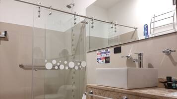 Un baño moderno con cabina de ducha de vidrio, inodoro blanco, lavamanos con encimera de mármol y espejo sobre el lavamanos.