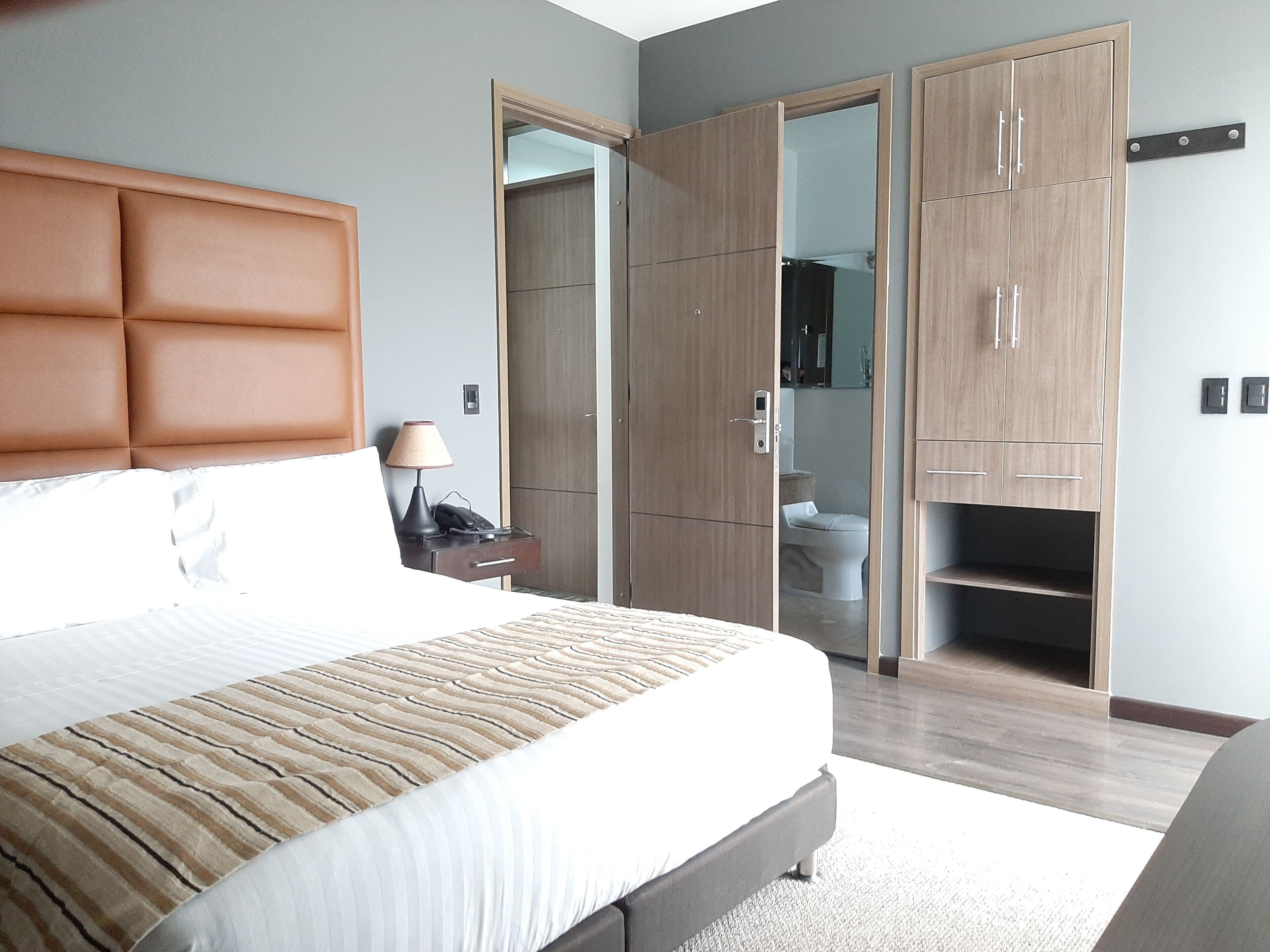 Una habitación de hotel moderna con una cama grande, un armario y un baño visible a través de una puerta abierta.