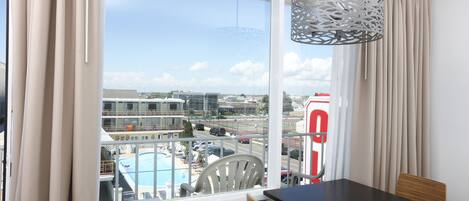 A balcony with a view of a swimming pool, a red and white building, and a clear sky.