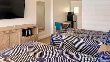 A hotel room with a large bed, a television, a small table, and a refrigerator.