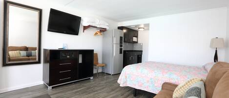 Una habitación de hotel con cama, cómoda, televisor, escritorio y kitchenette.