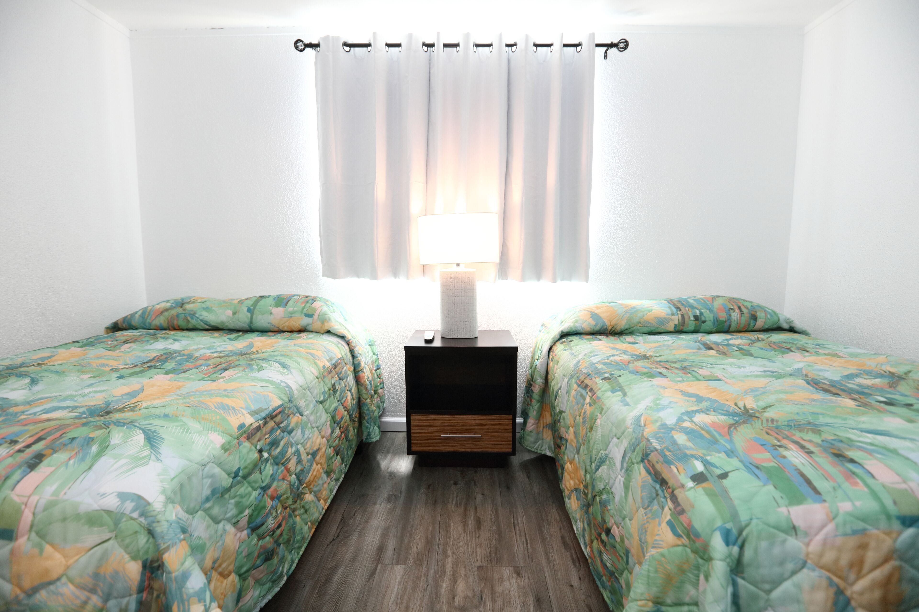 Une chambre avec deux lits, une table de chevet avec une lampe et une fenêtre avec des rideaux.
