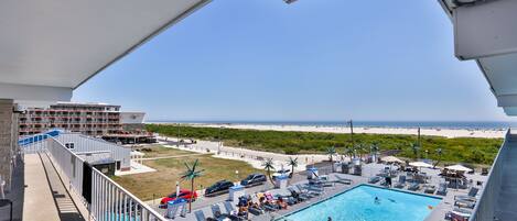 A pool area with lounge chairs, a swimming pool, and a view of the beach.