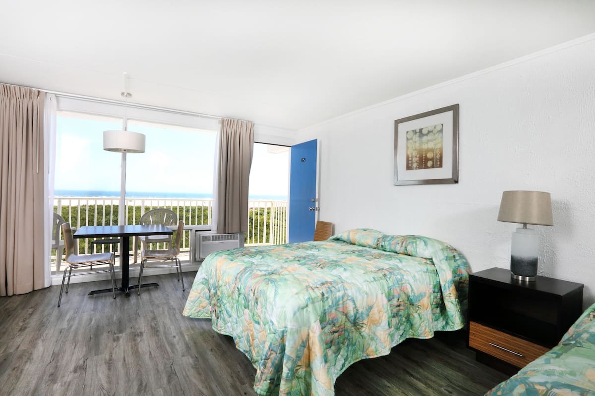 Ein Schlafzimmer mit einem Bett, einem Schreibtisch und einem Stuhl. Es gibt ein Fenster mit Vorhängen, eine Tür und ein Bild an der Wand.