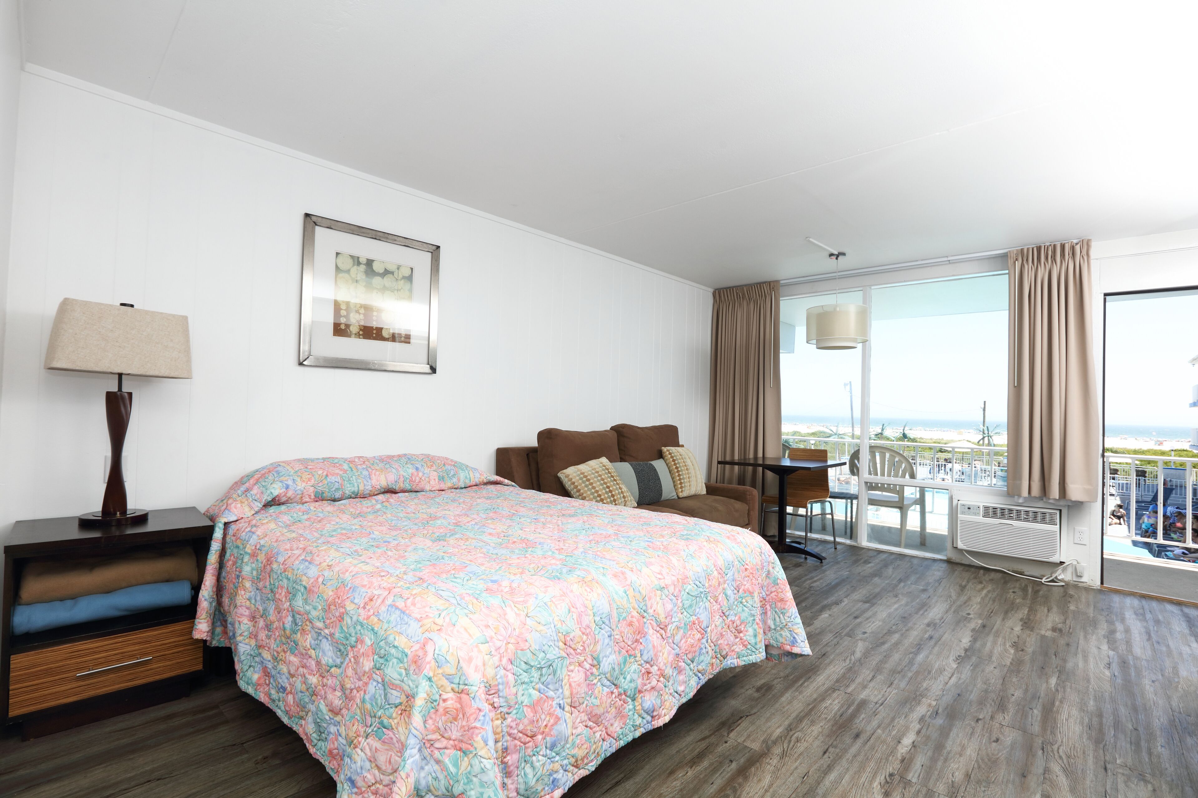 A hotel room with a large bed, a desk, a chair, a window with curtains, and a view of the ocean.