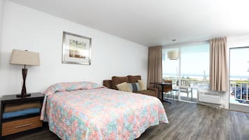 Habitación de hotel con una cama grande, un escritorio, una silla, una ventana con cortinas y vista al océano.