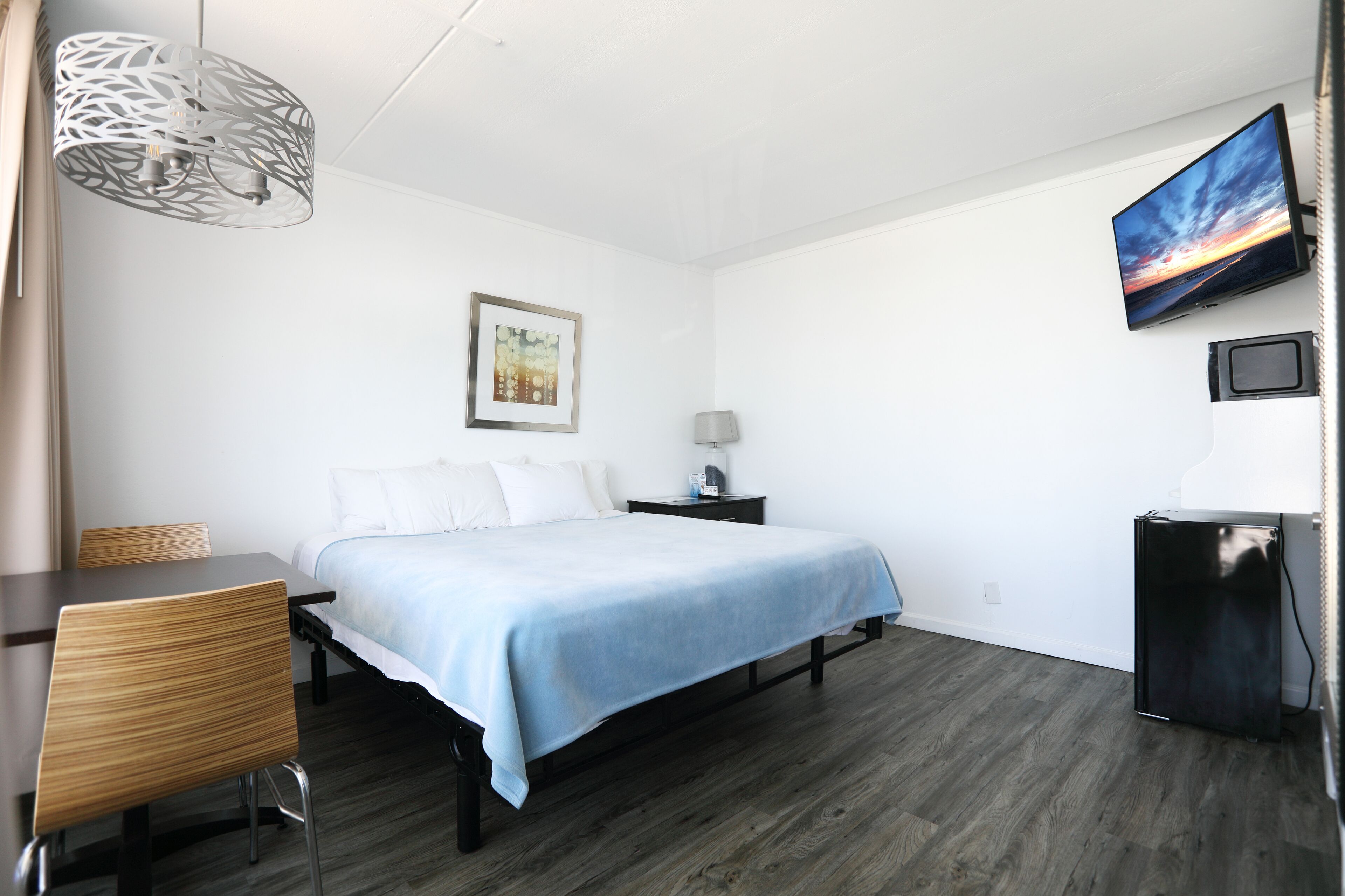 Une chambre d’hôtel comprenant un lit, un bureau, une chaise, une télévision et une petite table avec une lampe.