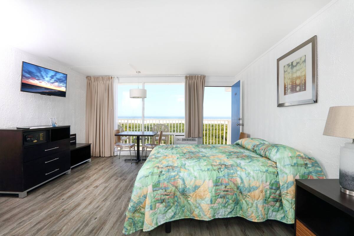 Ein Hotelzimmer mit Bett, Schreibtisch, Fernseher und einem Balkon mit Blick.