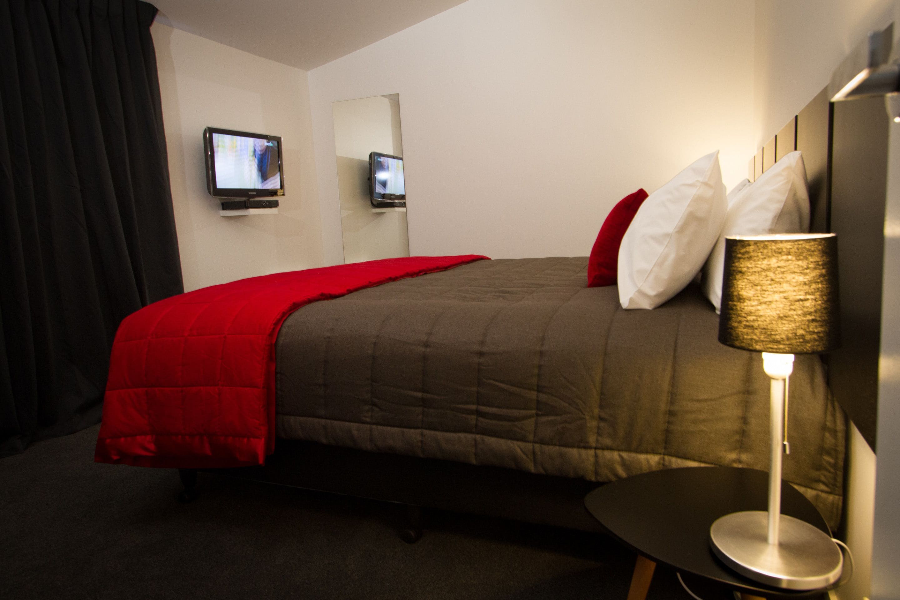 Une chambre d’hôtel avec un lit, une télévision, une lampe et une petite table.