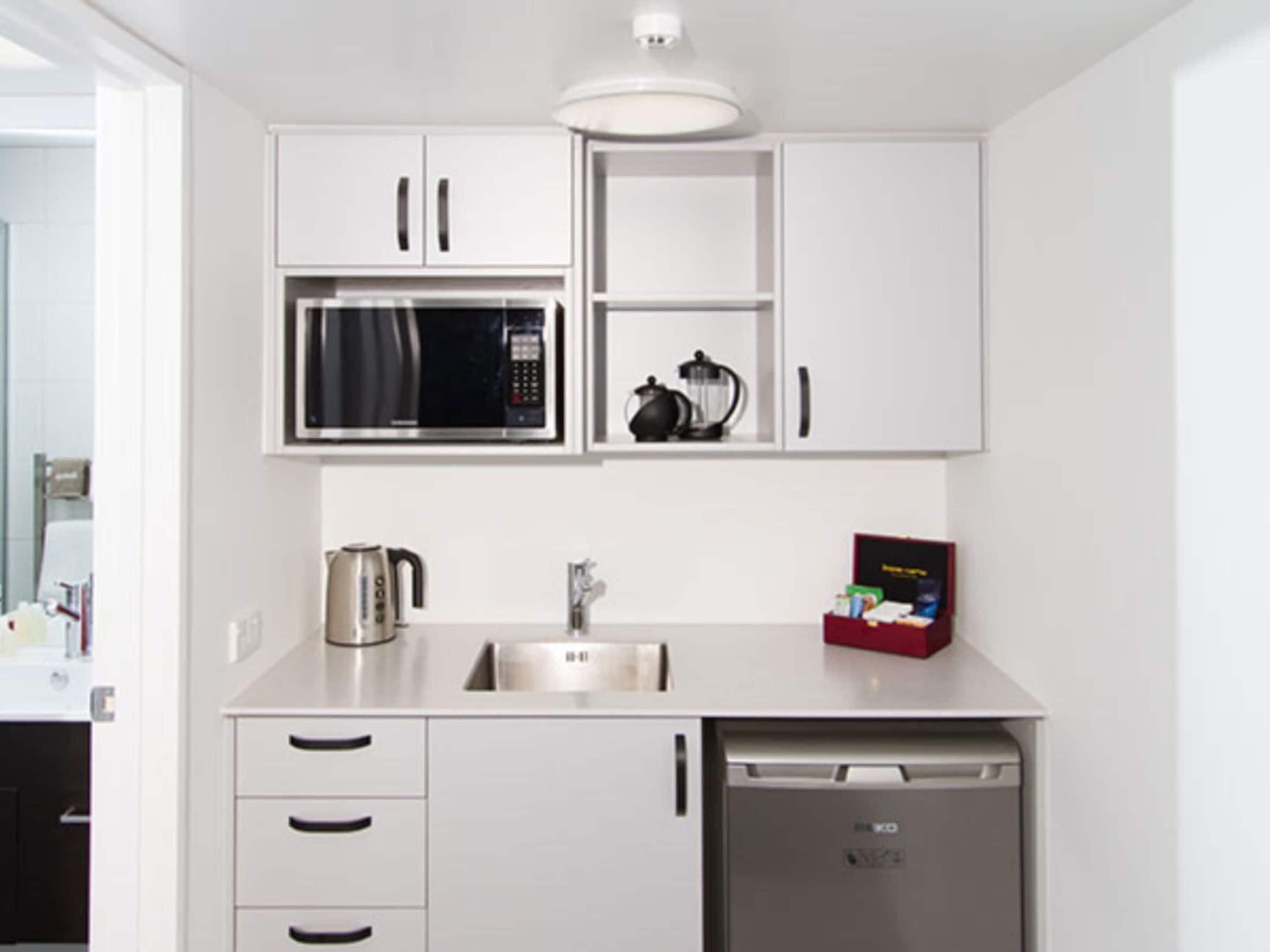 A compact kitchen with white cabinets, a microwave, a coffee maker, and a dishwasher.