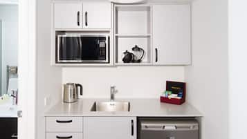 A compact kitchen with white cabinets, a microwave, a coffee maker, and a dishwasher.