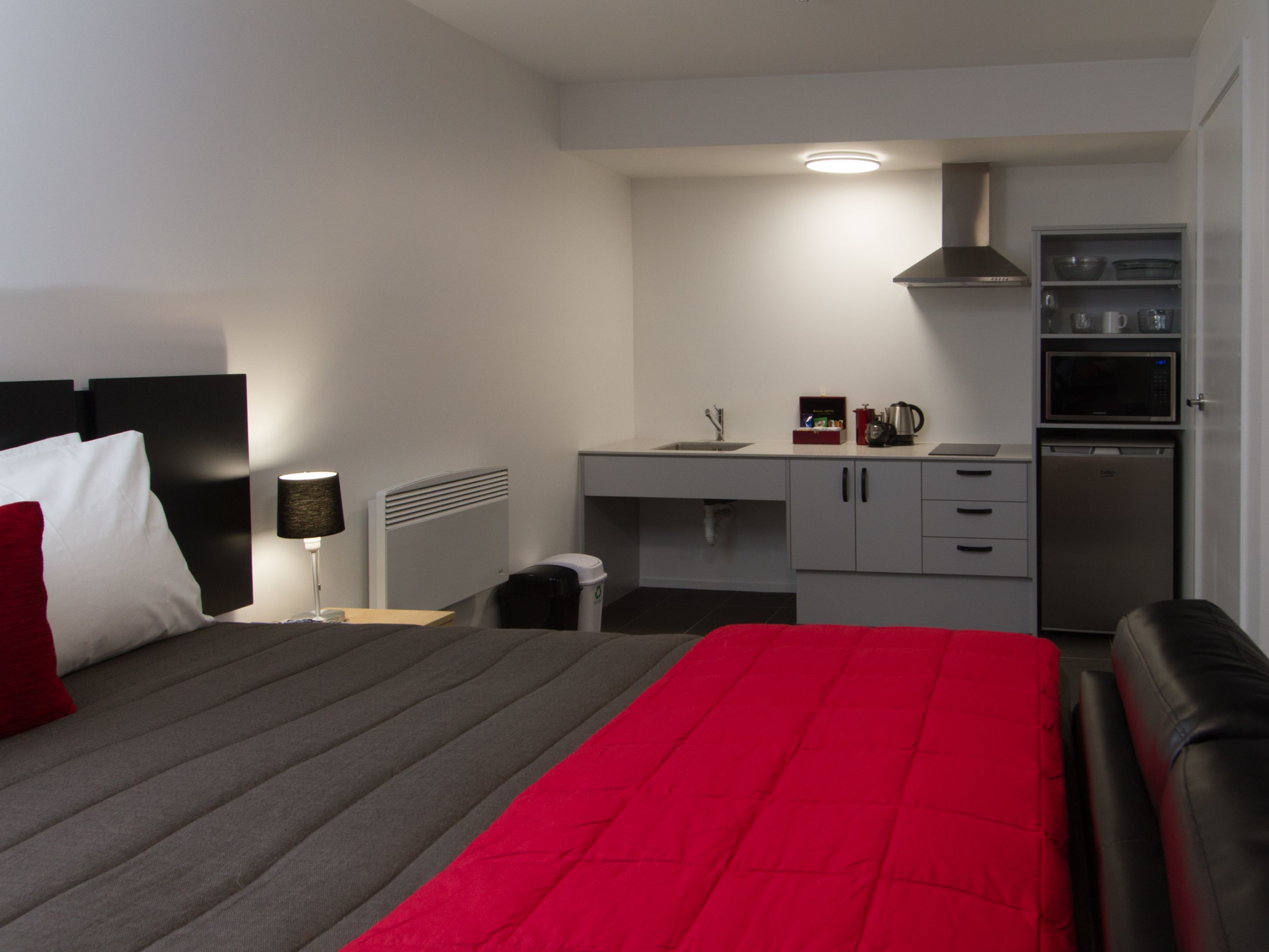 A hotel room with a bed, a desk, a kitchenette, and a bathroom.