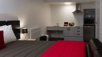 A hotel room with a bed, a desk, a kitchenette, and a bathroom.