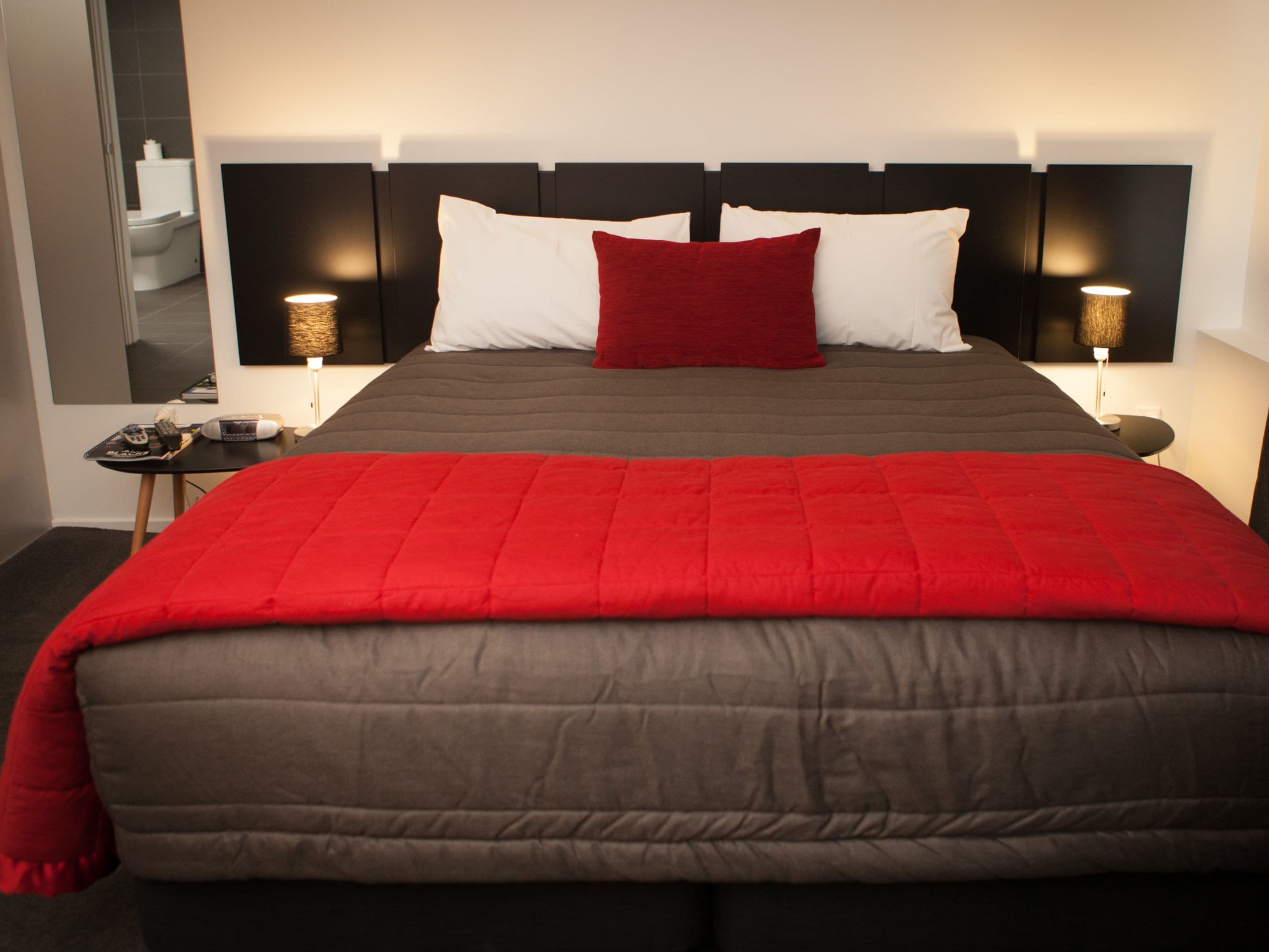 Una habitación de hotel con una cama grande, una mesita de noche, una lámpara y un espejo.