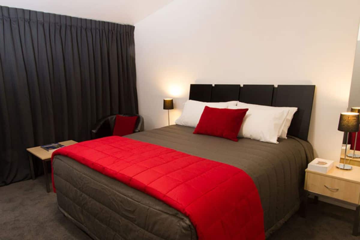 Quarto de hotel com cama, mesa de cabeceira, cadeira, escrivaninha e abajur.