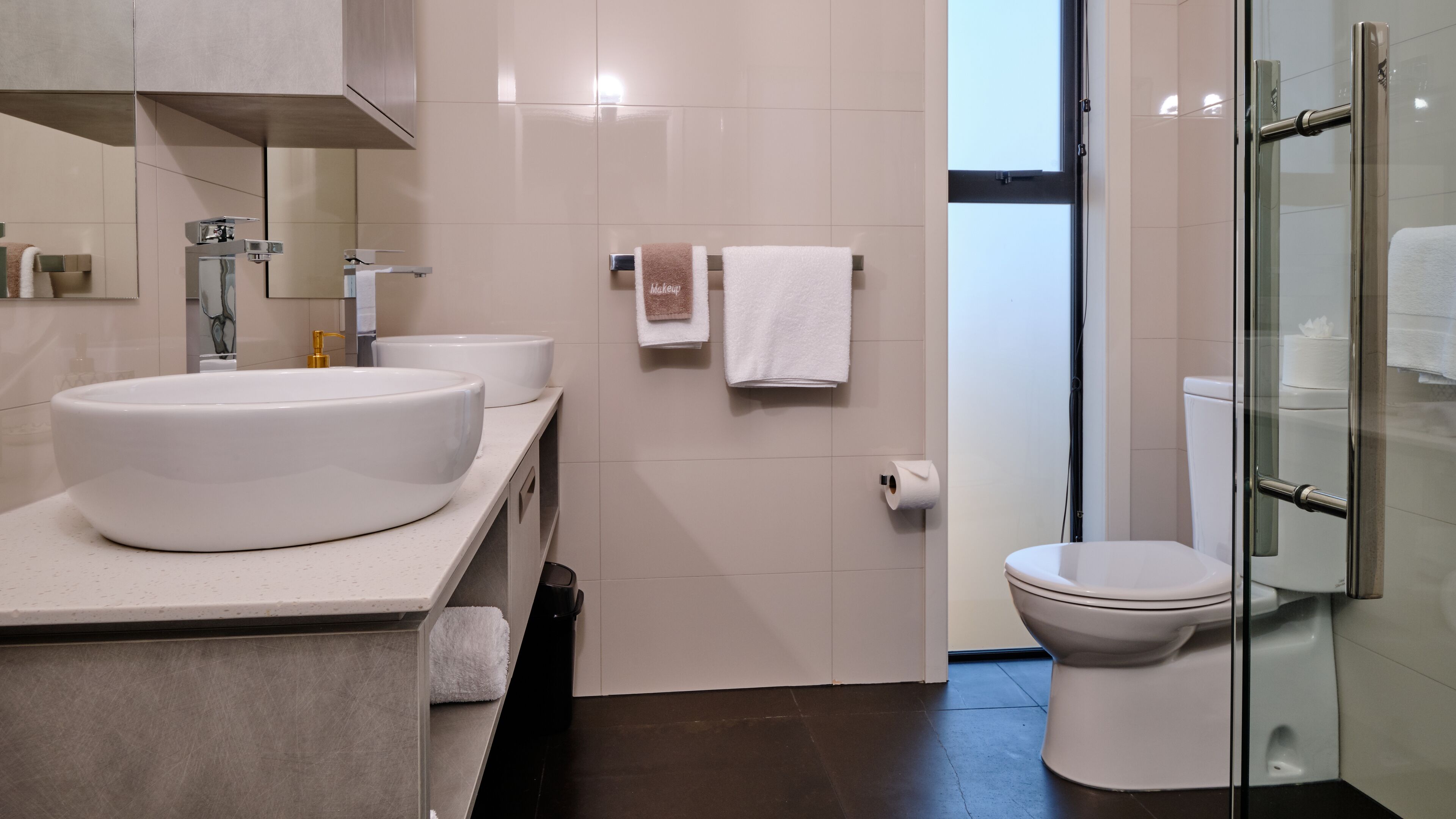 A modern bathroom with a large white sink, two white toilets, and a glass shower enclosure.