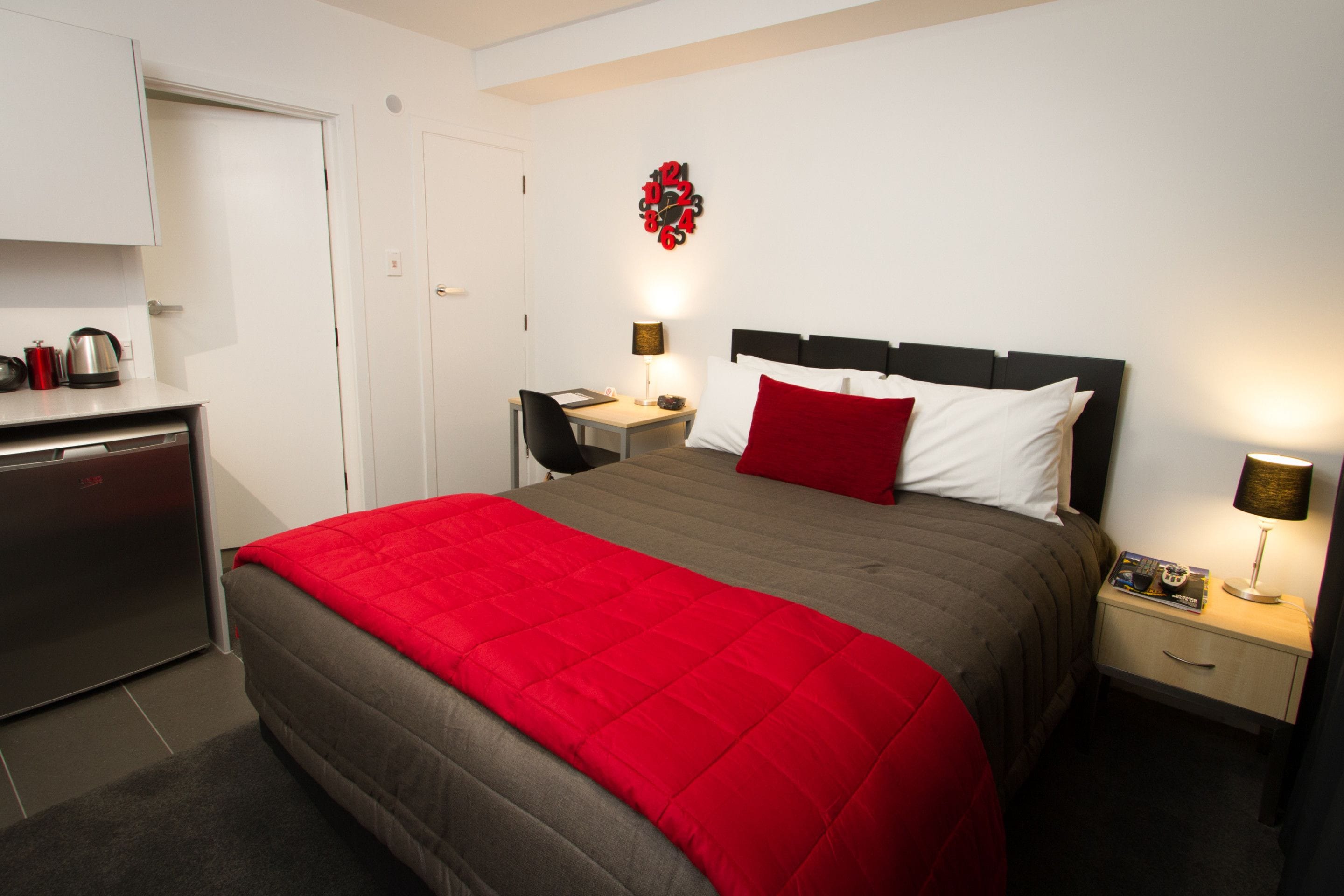 Ein Hotelzimmer mit Bett, Schreibtisch, Stuhl, Kleiderschrank und einer kleinen Küchenzeile.