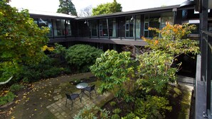 Un patio con un edificio de vidrio, una mesa pequeña con sillas y diversas plantas.