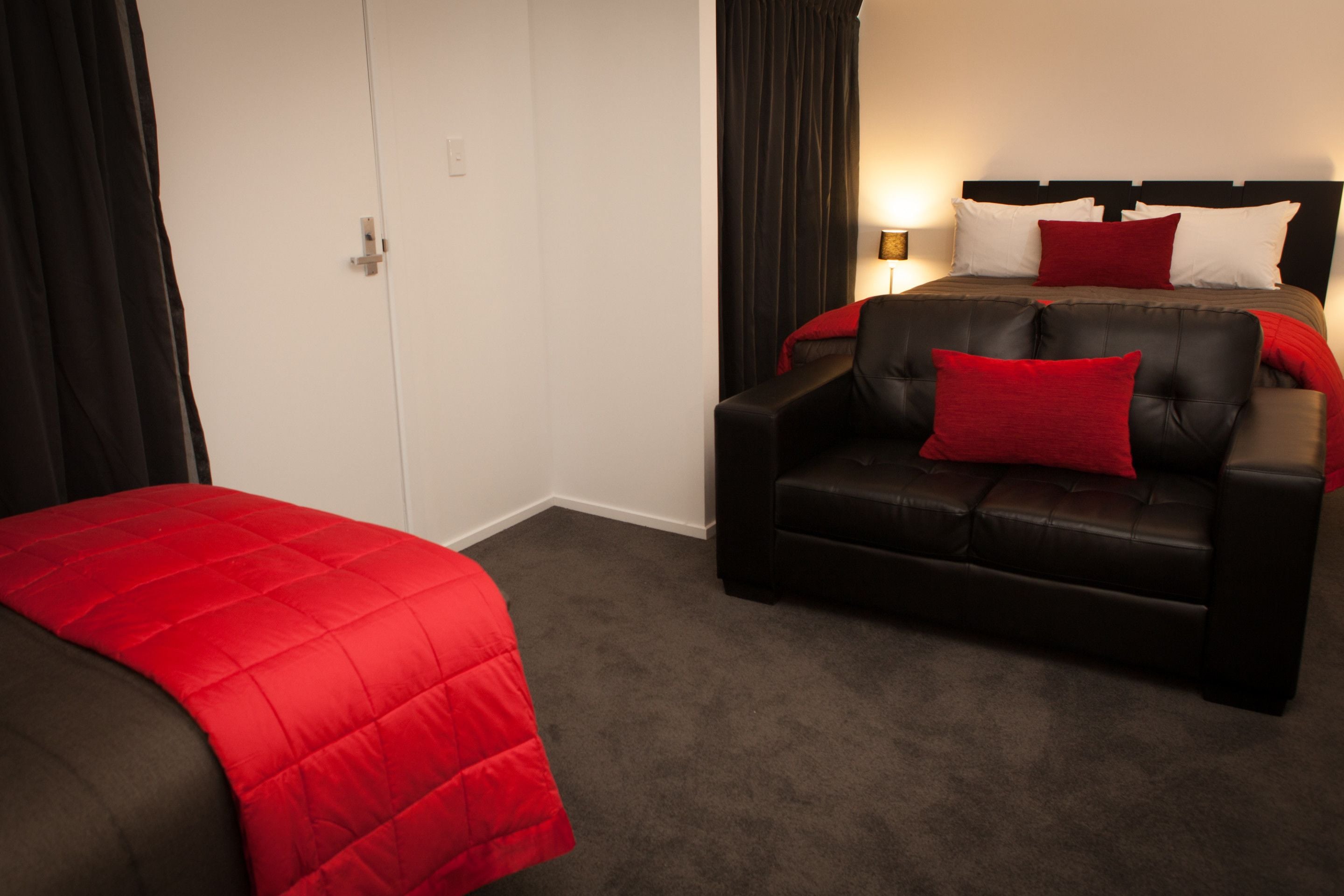 A hotel room with a bed, a black leather sofa, and a red blanket.