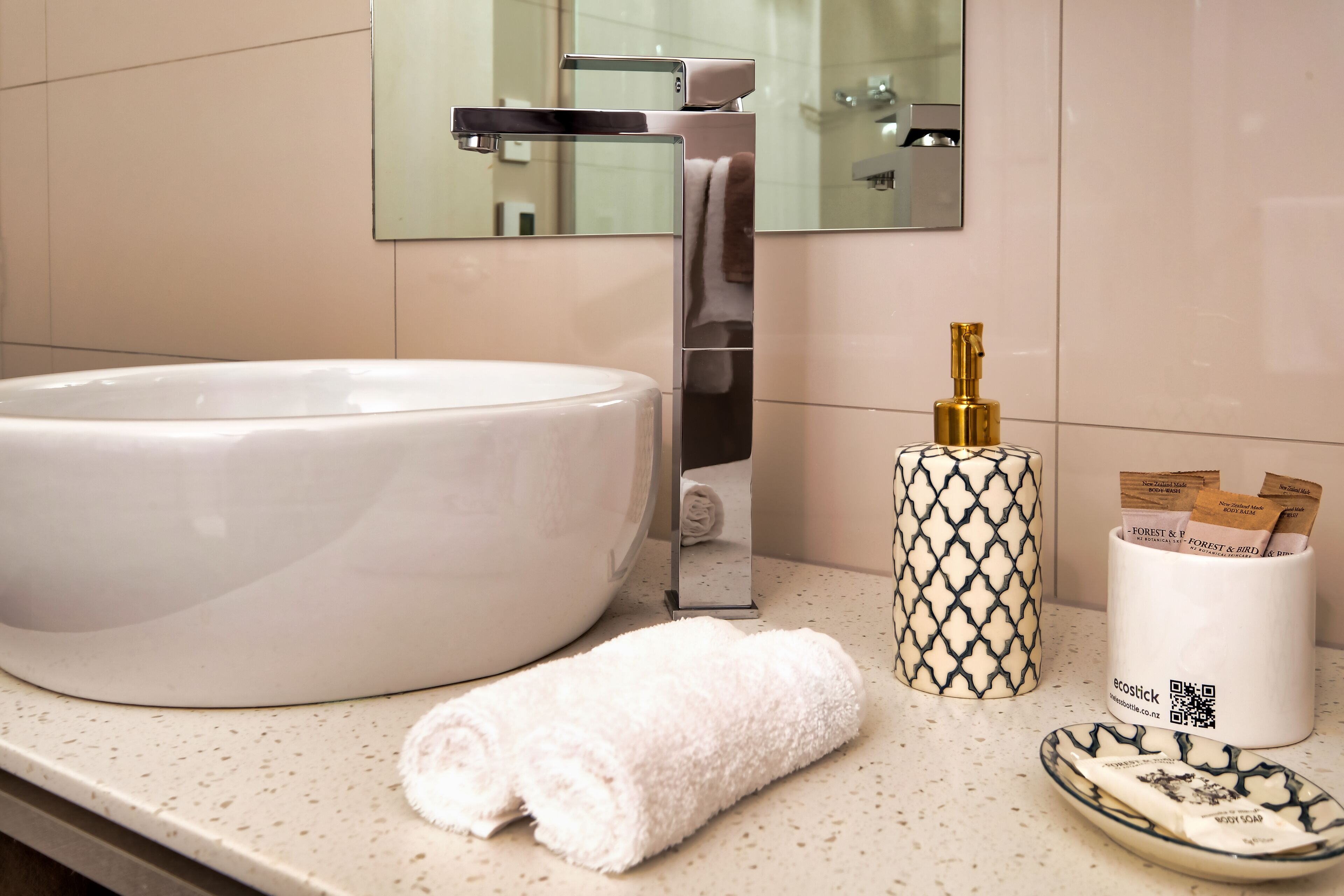 A bathroom with a large white sink, a towel, a patterned candle holder, and a tray with toiletries.