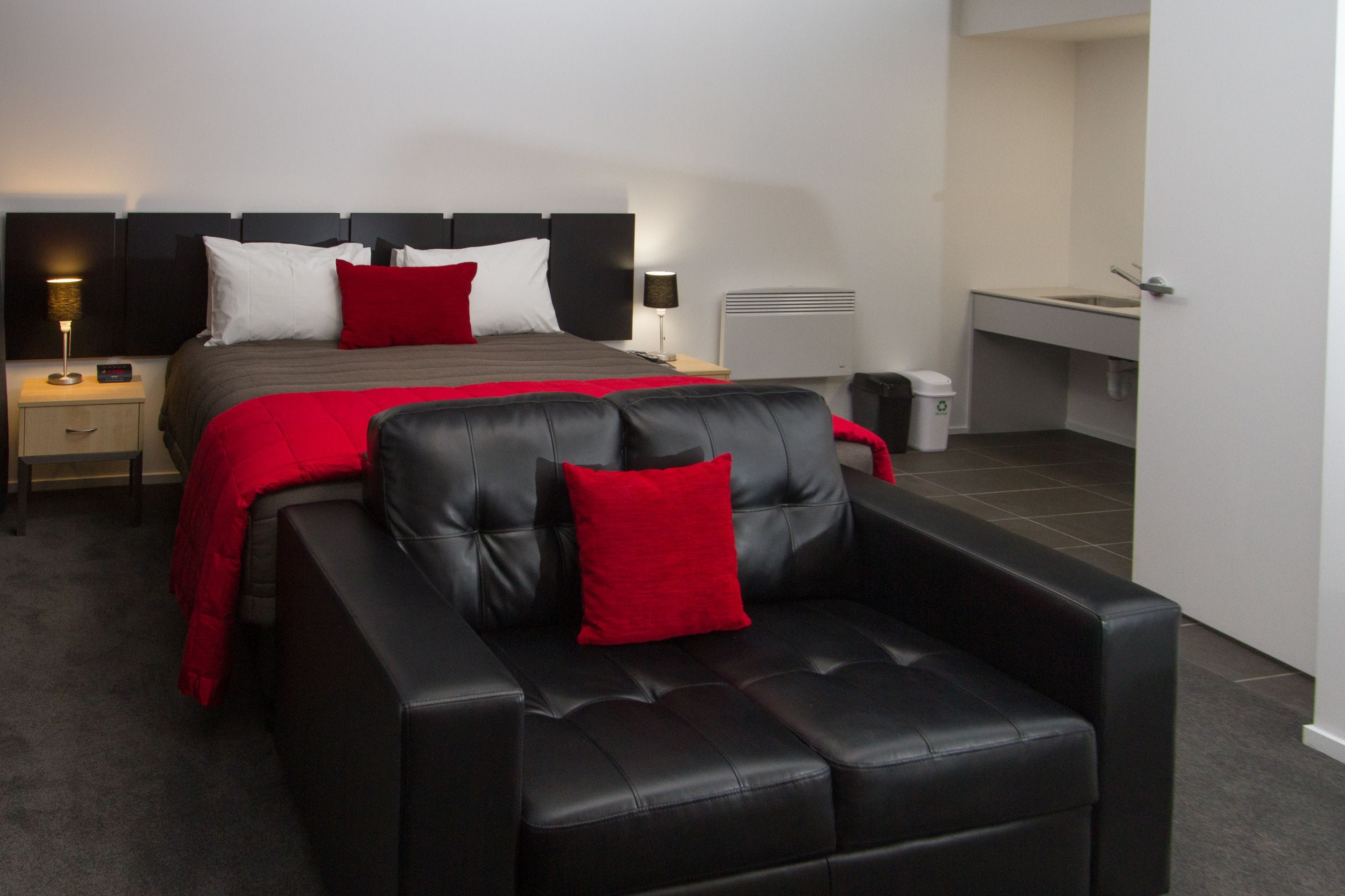 Une chambre d’hôtel moderne avec un grand lit, un canapé en cuir et un petit espace bureau.