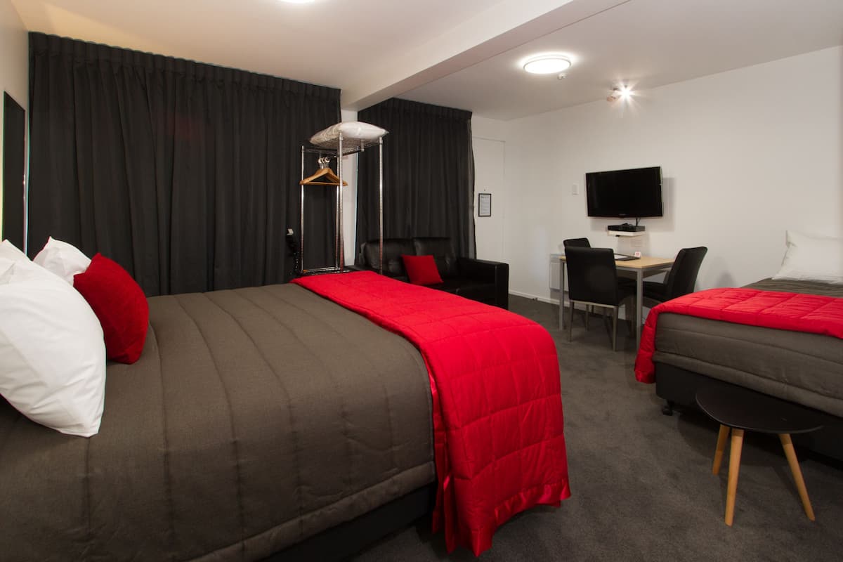 Quarto de hotel com duas camas, uma escrivaninha, uma cadeira, uma televisão e um guarda-roupa.