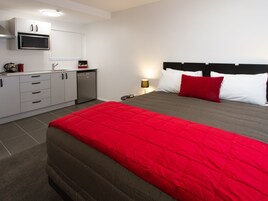 Una habitación de hotel moderna con una cama, una kitchenette pequeña y una mesita de noche con una lámpara.