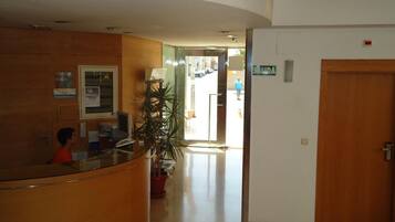Un área de recepción con un mostrador curvo, una recepción, una planta en maceta y una puerta que dice "SALIDA".