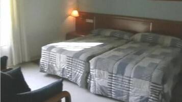 A hotel room with two beds, a nightstand, a chair, and a lamp.