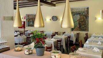 A restaurant with tables set for dining, pendant lights, and a painting on the wall.