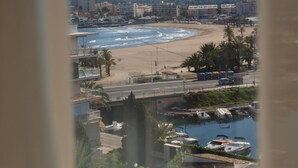 Un paisaje urbano costero con una playa, un puerto deportivo y edificios al fondo.
