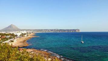 A coastal town with a clear view of the sea, a prominent mountain in the background, and a sailboat on the water.