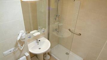 Un baño moderno con ducha envuelta en vidrio, lavamanos pedestal y secador de pelo en la pared.