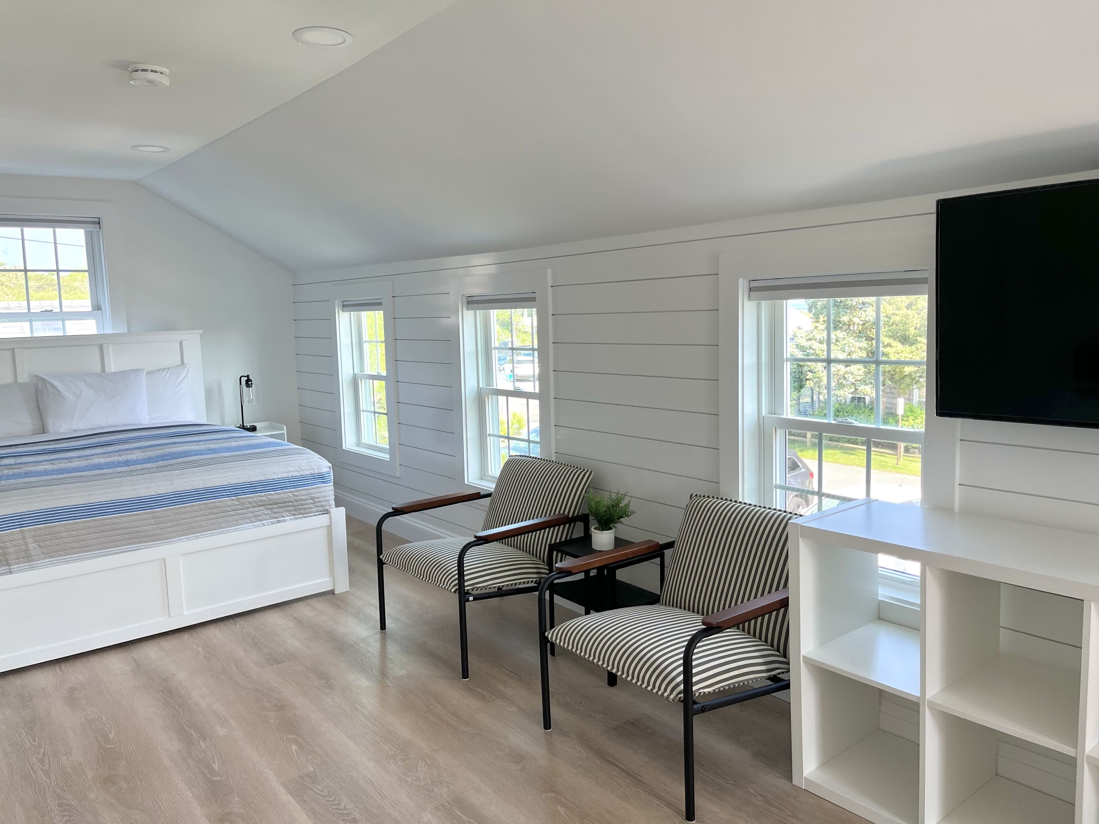 Un dormitorio con una cama, dos sillas, un televisor y un escritorio con estanterías.