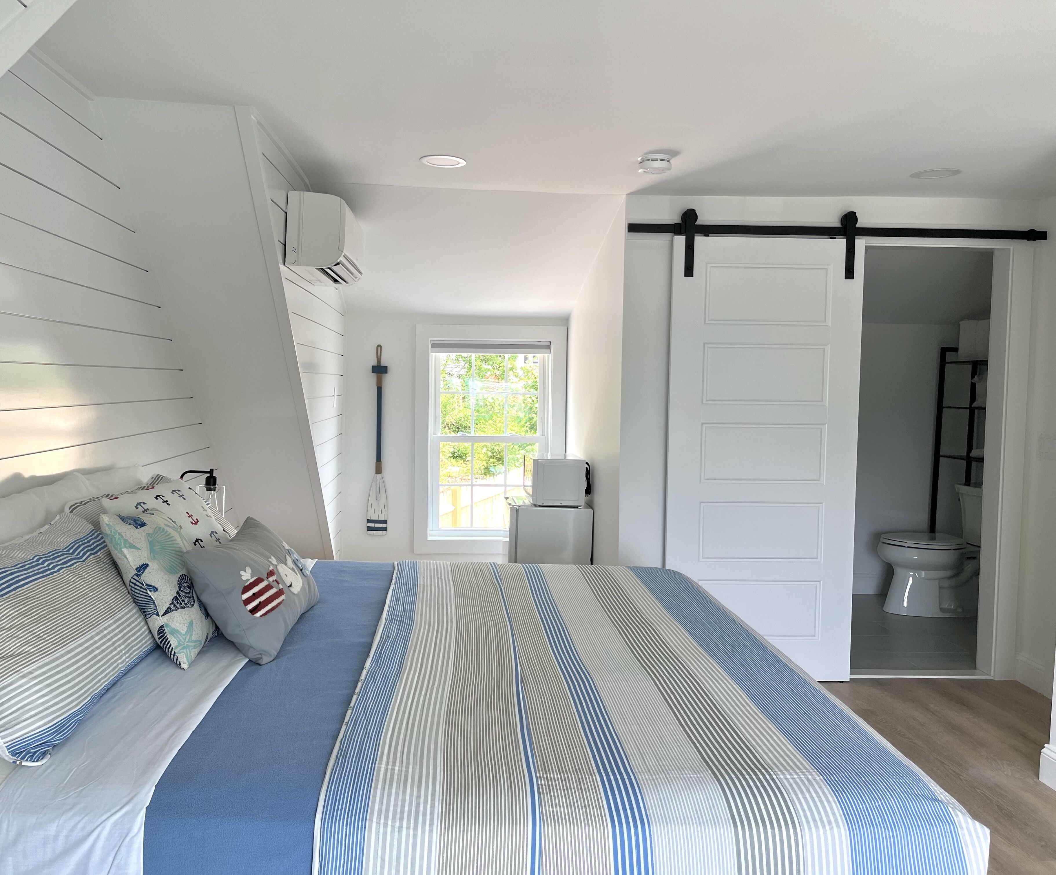 A bedroom with a bed, a window, a door, and a bathroom.