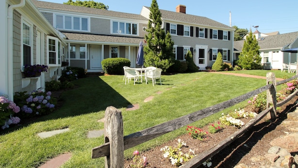Un immeuble résidentiel de deux étages doté d’une pelouse bien entretenue, d’une clôture en bois et d’un espace patio aménagé avec du mobilier d’extérieur.